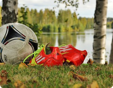 Fotboll och fotbollsskor i gräset framför sjö.